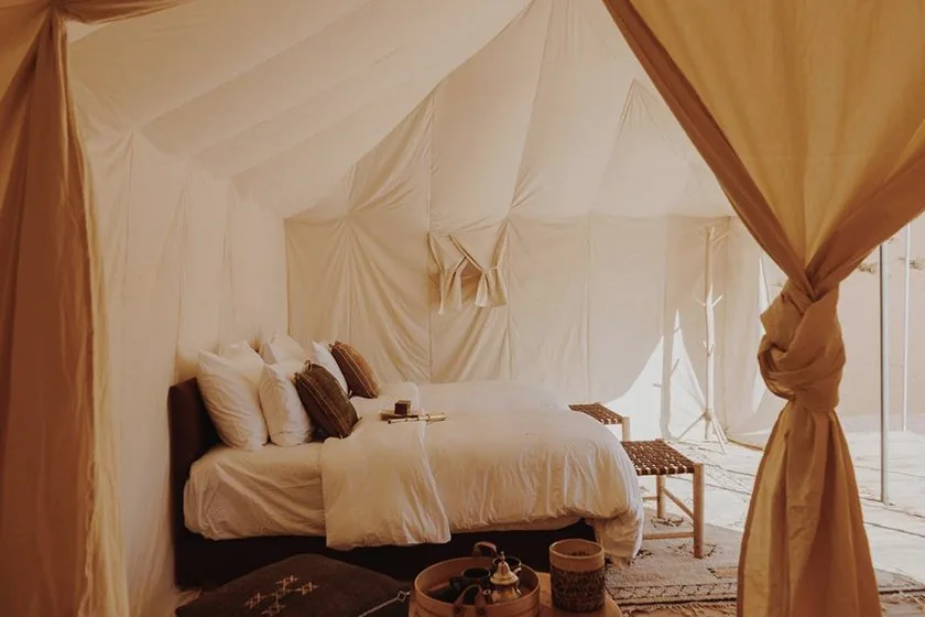 The inside of a canvas tent in the Moroccan desert, with a made bed and a tea tray